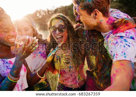 cheerful young multiethnic friends with colorful paint on clothes and bodies having fun together at holi festival 