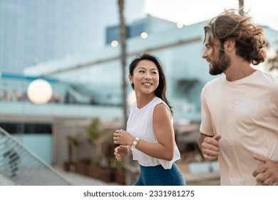 Cheerful young multi-ethnic urban couple running alongside beach wearing casual summer sport clothing. Jogging in the city - Powered by Shutterstock