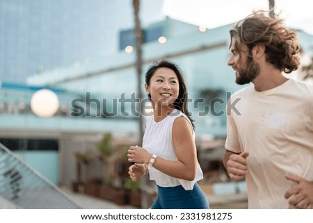 Cheerful young multi-ethnic urban couple running alongside beach wearing casual summer sport clothing. Jogging in the city