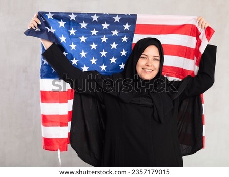 Cheerful young muslim woman wearing black traditional hijab holding flag of usa