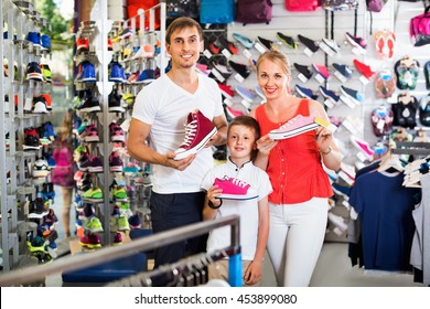 Cheerful young parents with boy in school age shopping shoes in sport store