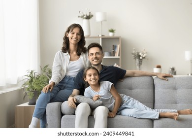 Cheerful young parents and cute tween girl kid relaxing together on soft couch at cozy home, looking at camera with toothy smiles, enjoying leisure in stylish new apartment. Family portrait - Powered by Shutterstock