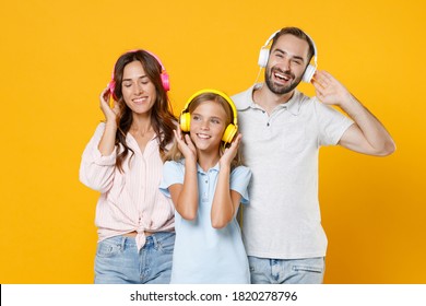 Cheerful young parents mom dad with child kid daughter teen girl in basic t-shirts listen music with headphones isolated on yellow background studio portrait. Family day parenthood childhood concept - Powered by Shutterstock