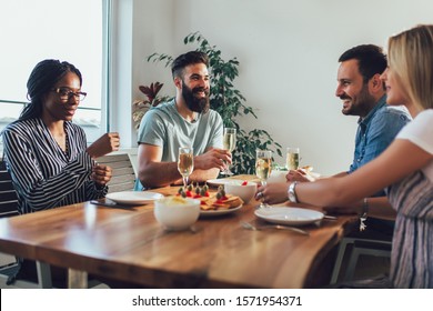 Cheerful young people enjoying meal while sitting at the dinning table on the kitchen together.