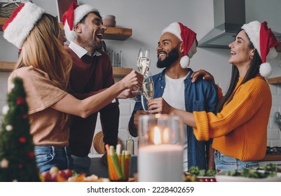 Cheerful young people toasting with champagne while enjoying Christmas dinner at home - Shutterstock ID 2228402659