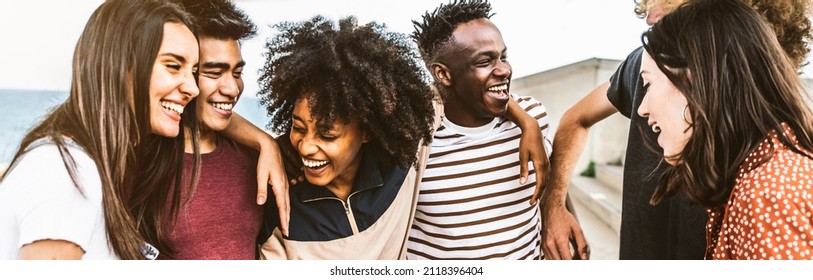Cheerful young people walking outside talking and having fun - Mixed race friends hanging down the street - Group of teenagers having party celebrating laughing out loud - Youth lifestyle concept - Shutterstock ID 2118396404