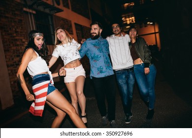 Cheerful Young People Walking Together At Night And Having Fun. Multiracial Group Of Friends Hanging Out In Evening.