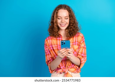 Cheerful young red-haired woman using smartphone against a vibrant blue background, expressing joy and curiosity with a casual and friendly vibe - Powered by Shutterstock