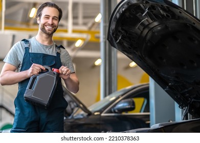 Cheerful Young Service Station Worker Changing The Motor Oil