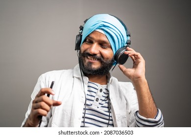 Cheerful young sikh man dancing while listening music on Headphone by using mobilephone- concept of joyful emotion and Happiness