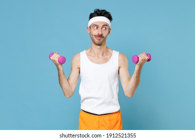 Cheerful Young Strong Sporty Fitness Man With Thin Skinny Body Sportsman In White Headband Shirt Shorts Doing Exercise With Dumbbells Isolated On Blue Background. Workout Gym Sport Motivation Concept