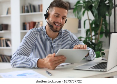 Cheerful young support phone male operator in headset, at workplace while using digital tablet