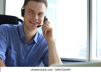 Cheerful Young Support Phone Male Operator In Headset, At Workplace While Using Laptop, Help Service And Client Consulting Call Center Concept.