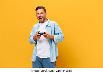 Cheerful young tanned handsome man in blue basic t-shirt play game hold joystick posing isolated on orange yellow studio background. Copy space Banner Mockup. People lifestyle Lucky winner concept