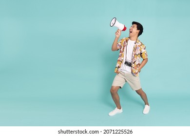 Cheerful young traveler tourist Asian man in summer clothes screaming in megaphone isolated on green background, Passenger traveling on long weekend, Full length composition