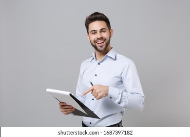 Cheerful Young Unshaven Business Man In Light Shirt Isolated On Grey Background. Achievement Career Wealth Business Concept. Mock Up Copy Space. Point Index Finger On Clipboard With Papers Document