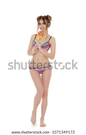 Cheerful young woman in bikini stands with lollipop on a white background. Pin up style.