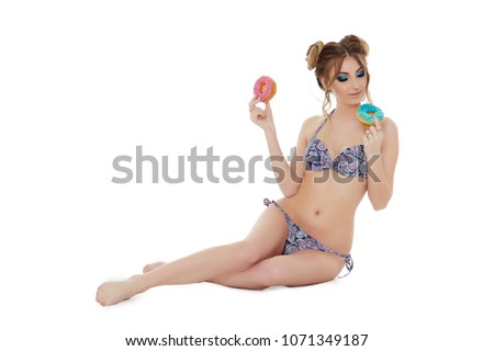 Cheerful young woman in bikini stands with donuts on a white background. Pin up style.