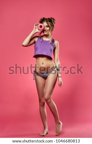 Cheerful young woman in bikini and top stands with tasty donut on a pink background. Pin up style.