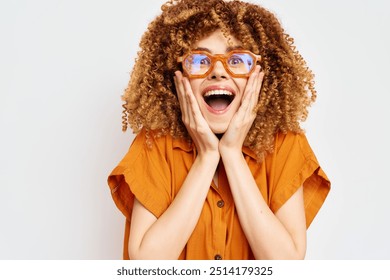 cheerful young woman with curly hair and orange shirt expressing amazement against a light background, showcasing joy and excitement in a playful manner - Powered by Shutterstock