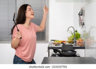 Cheerful Young Woman Dancing While Cooking Food In The Kitchen At Home