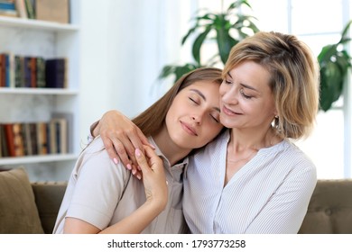 Eine fröhliche junge Frau umarmt ihre Mutter mittleren Alters im Wohnzimmer.