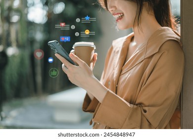 A cheerful young woman engaging with social media on her smartphone, receiving likes and reactions while holding a coffee cup outdoors - Powered by Shutterstock