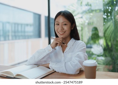 A cheerful young woman enjoys a coffee while contemplating ideas at a wooden table, surrounded by plants and natural light, creating a peaceful and inspiring workspace ambiance. - Powered by Shutterstock