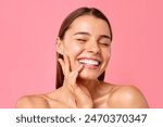 A cheerful young woman flashes a bright smile against a pink backdrop, showcasing her clear, radiant skin and natural beauty. Perfect for wellness, skincare, and positivity concepts.