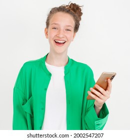 Cheerful Young Woman Girl In Green Shirt Posing Isolated On Gray Wall Background Studio Portait. People Lifestyle Concept. Happy Teen Using Mobile Phone Typing Sms Message Winer