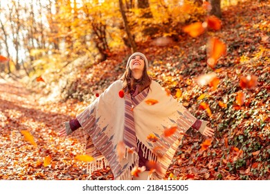 Cheerful young woman having fun spending sunny autumn day in nature, looking up with arms spread, watching the colorful leaves fall on the forest path - Powered by Shutterstock