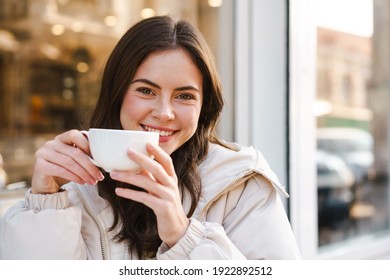 Cheerful young woman having tea with cake at the cafe outdoors