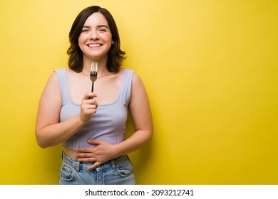 Cheerful Young Woman Holding A Fork After Eating And Feeling Full With Food While Rubbing Her Stomach 