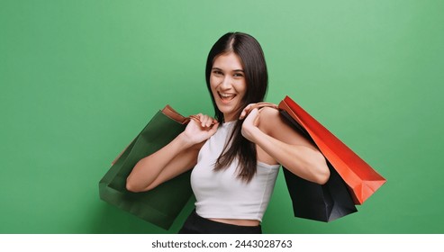 Cheerful young woman holding shopping bags. Isolated on green background in studio. - Powered by Shutterstock