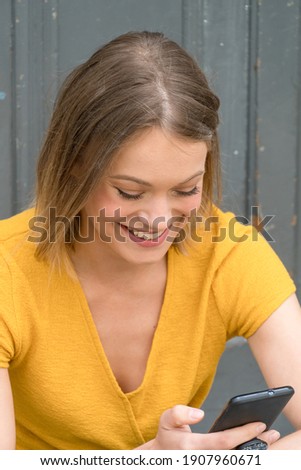 Cheerful young woman holding a smartphone while sitting outdoors