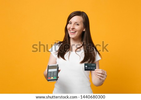Cheerful young woman holding wireless modern bank payment terminal to process and acquire credit card payments isolated on yellow orange wall background. People lifestyle concept. Mock up copy space
