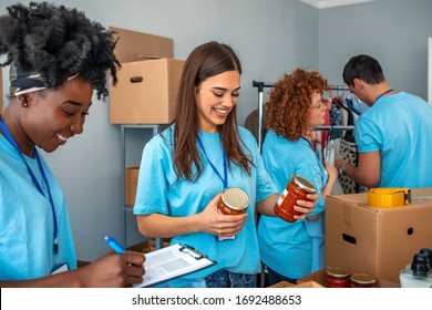 Cheerful young woman laughs along with her friend while volunteering in a community food bank. They are sorting through food donations. Volunteers are working in the background