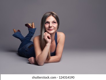 Cheerful Young Woman Laying Down On The Floor And Smiling.on Grey Background