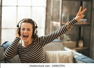 Cheerful young woman listening music in headphones in loft apartment