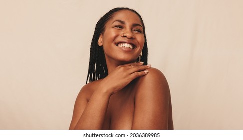 Cheerful young woman looking away with a smile on her face. Happy young woman standing naked against a studio background. Confident young woman embracing her natural body and beauty.