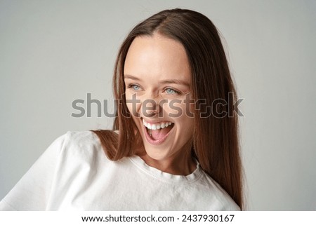 Cheerful young woman looking at camera smiling laughing over gray background