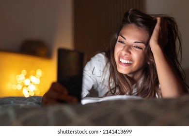 Cheerful young woman lying in bed at night, having video call using smart phone - Shutterstock ID 2141413699