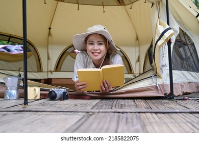 Cheerful Young Woman Lying In Her Camping Tent And Reading A Book. Travel, Camping And Vacation Concept