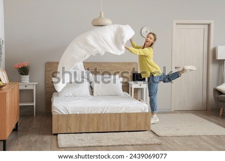Cheerful young woman making bed in modern bedroom