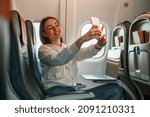 Cheerful young woman making selfie in airplane