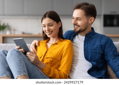 Cheerful young woman and man enjoy browsing on digital tablet together, shopping online or video calling, comfortably seated on couch in living room - Powered by Shutterstock