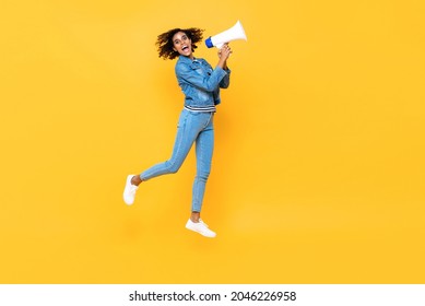 Cheerful young woman with megaphone jumping on yellow color studio background - Shutterstock ID 2046226958