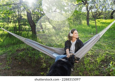 Cheerful young woman on a hammock in a summer garden communicating with a pet dog. Summer lifestyle and country life - Powered by Shutterstock