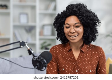 Cheerful young woman podcasting with microphone at home, expressing positivity and confidence in a cozy interior setting. - Powered by Shutterstock