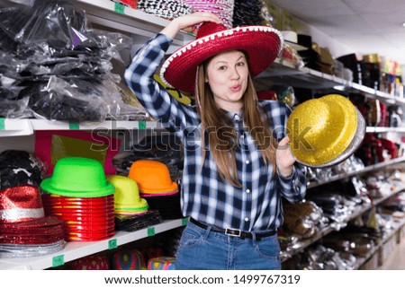 Cheerful young woman preparing for party, choosing funny headdresses in store